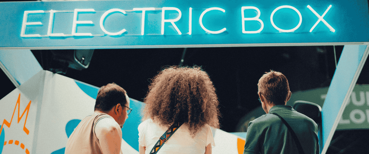 Trois personnes de dos devant un stand technologique avec enseigne lumineuse Electric Box lors d’un salon professionnel