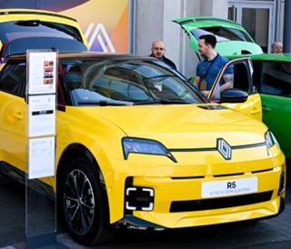 Une Renault R5 électrique jaune est exposée sur un stand automobile, capot ouvert, tandis que des visiteurs observent le véhicule et lisent les informations techniques.