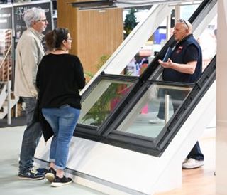 Un exposant présente une fenêtre de toit à deux visiteurs sur un stand du salon.