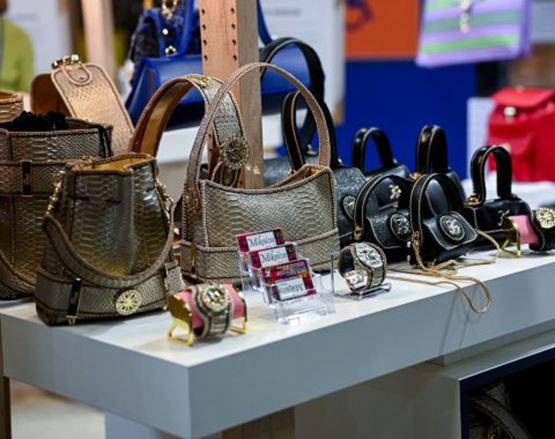 Exposition de sacs à main en cuir, avec des modèles dorés, noirs et rouges, accompagnés de montres et accessoires sur un comptoir.