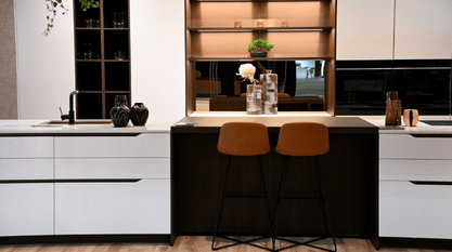 Cuisine design blanche avec ilot central et coin repas avec tabourets marron.