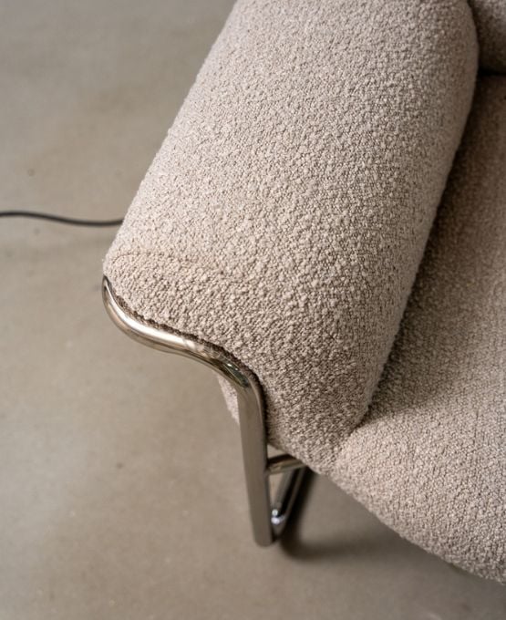 Gros plan sur accoudoir de fauteuil en tissu bouclé beige avec structure métallique, design moderne et minimaliste