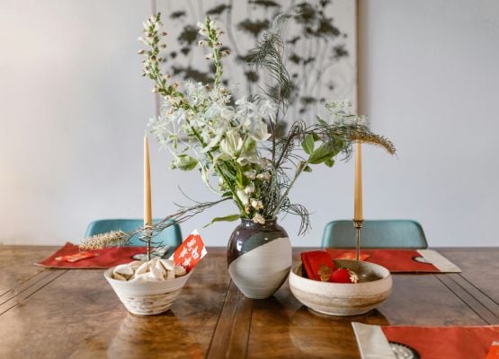 Table en bois décorée avec vase de fleurs, bougies fines et assiettes, ambiance élégante et naturelle dans une salle à manger