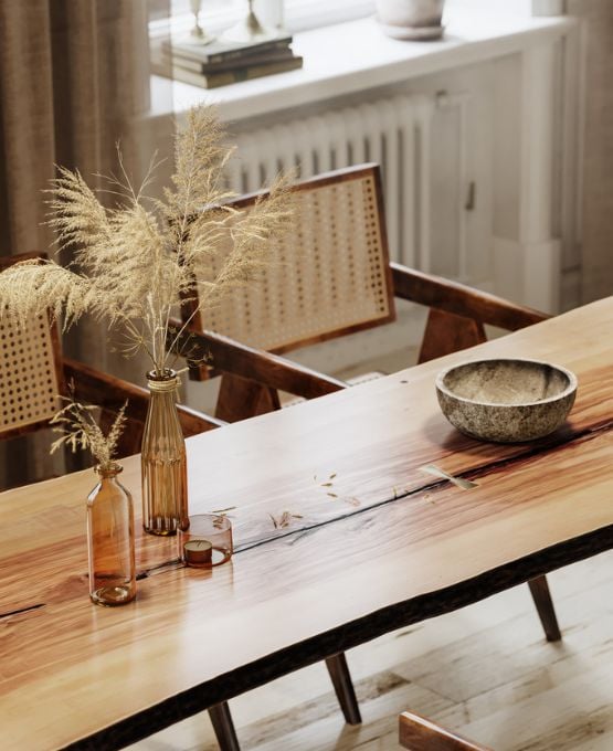 Table en bois massif avec vases en verre et herbes séchées, bol décoratif et chaises cannage dans une ambiance chaleureuse