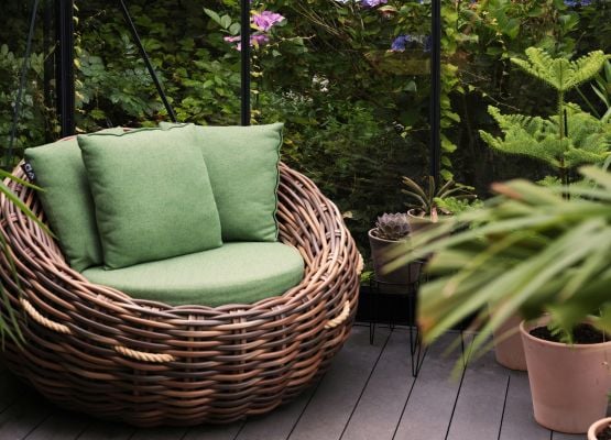 Fauteuil rond en rotin avec coussins verts sur une terrasse entourée de plantes, dans une ambiance naturelle et apaisante