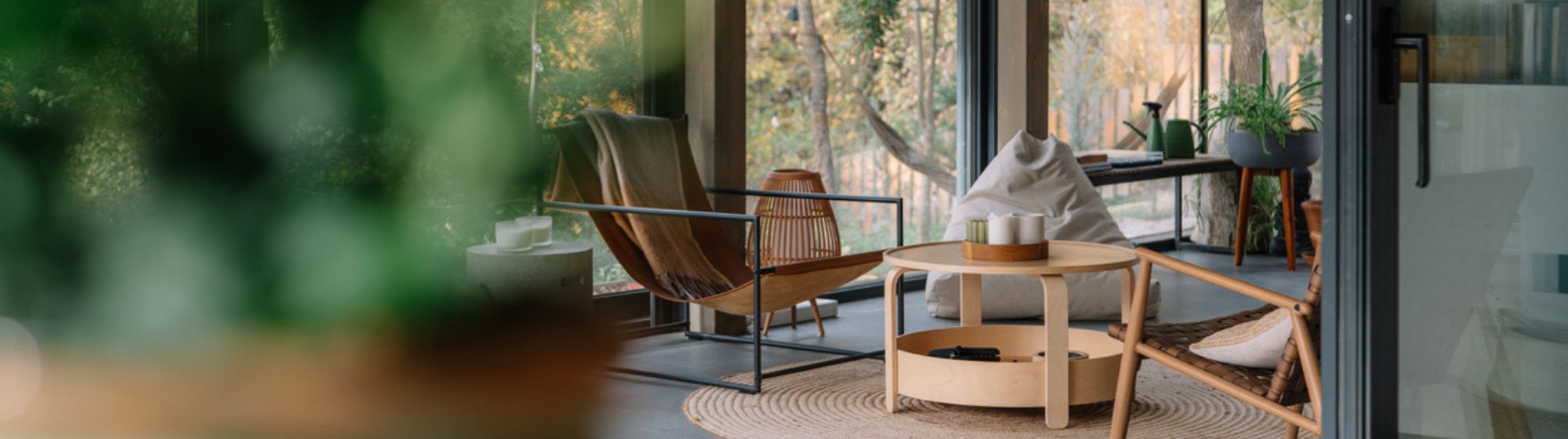 Salon lumineux avec grandes baies vitrées donnant sur la nature, mobilier en bois et décoration minimaliste.