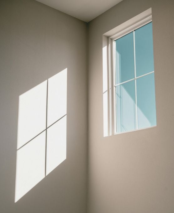 Fenêtre laissant entrer la lumière avec ombre géométrique projetée sur un mur blanc.