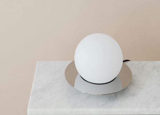 Lampe design sphérique blanche posée sur une base en marbre dans un intérieur épuré.