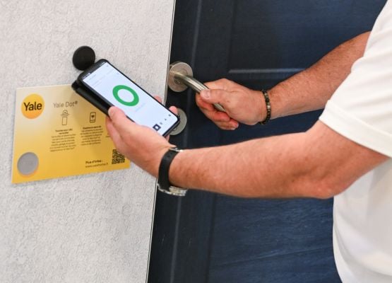 Personne déverrouillant une porte sécurisée avec un smartphone et un système connecté.