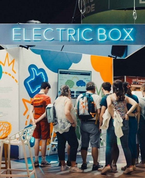 Visiteurs rassemblés devant le stand Electric Box observant un écran dans un salon d’exposition.